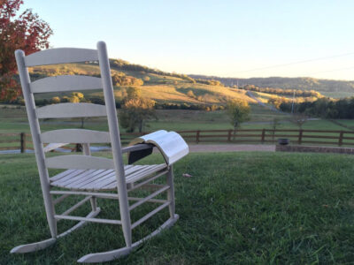 A rocking chair with a book laid on the arm, looking out over beautiful countryside